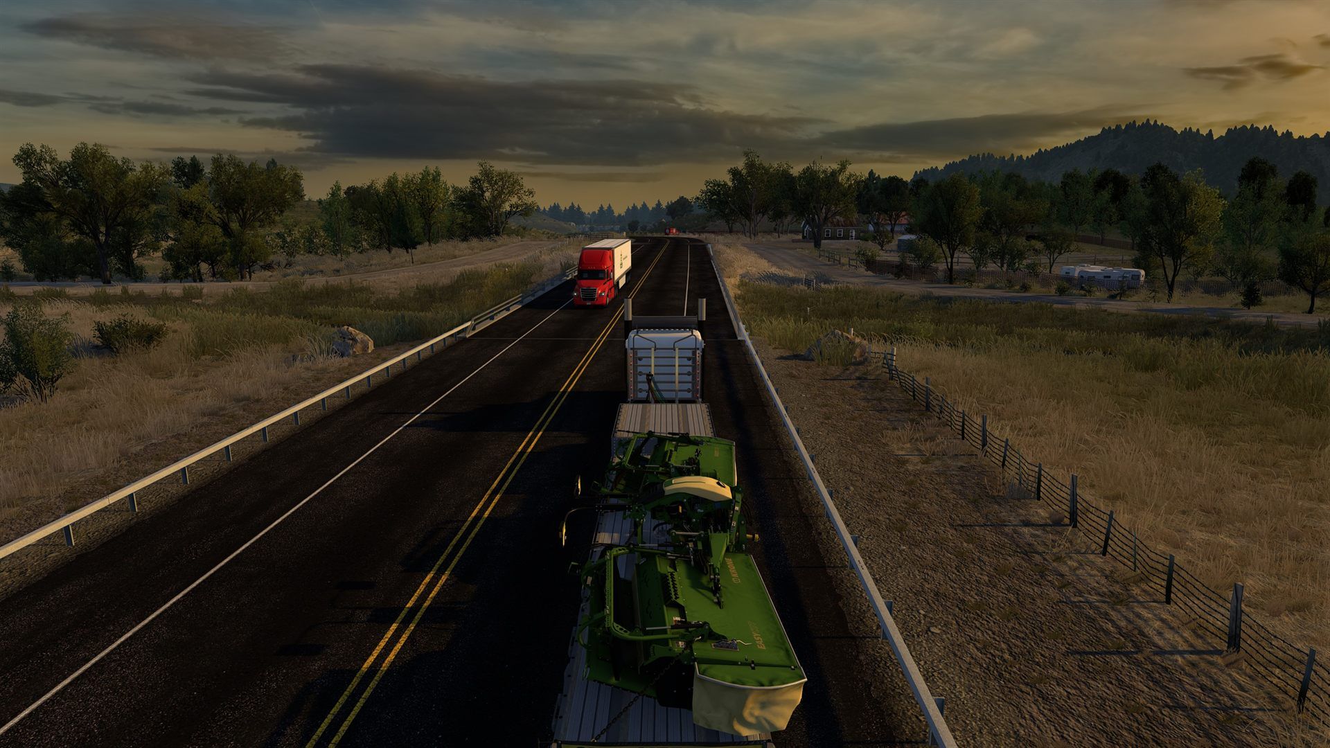 A red truck and a flatbed carrying a mower pass each other on a country road at sunset, in American Truck Simulator.